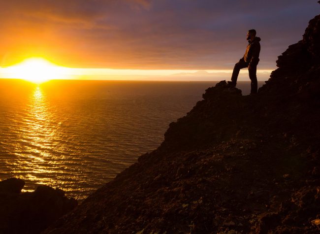 Lonely man standing on cliff edge rock staring at sunset with Te
